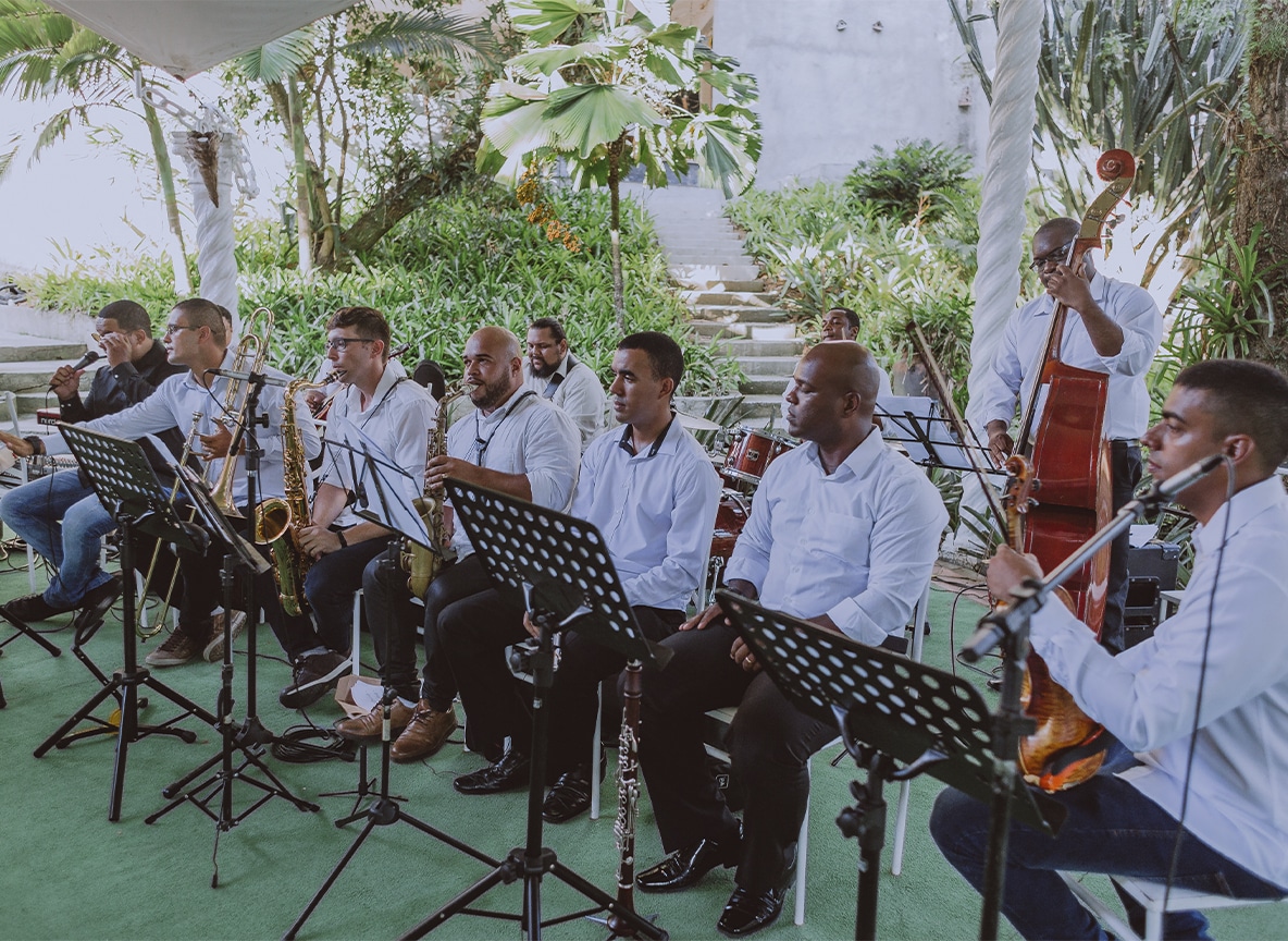 Orquestra de músicos tocando instrumentos como saxofone, violino e contrabaixo em cerimônia de casamento ao ar livre.