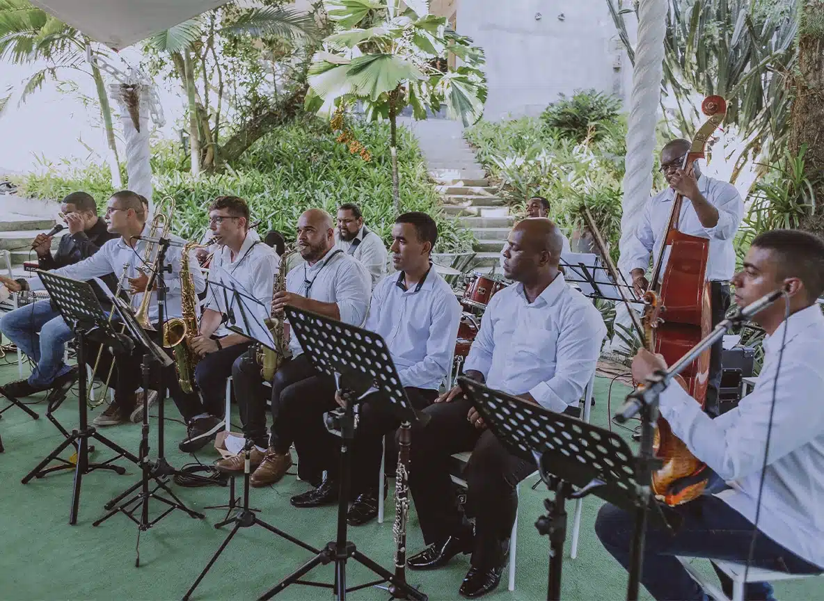 Orquestra de músicos tocando instrumentos como saxofone, violino e contrabaixo em cerimônia de casamento ao ar livre.